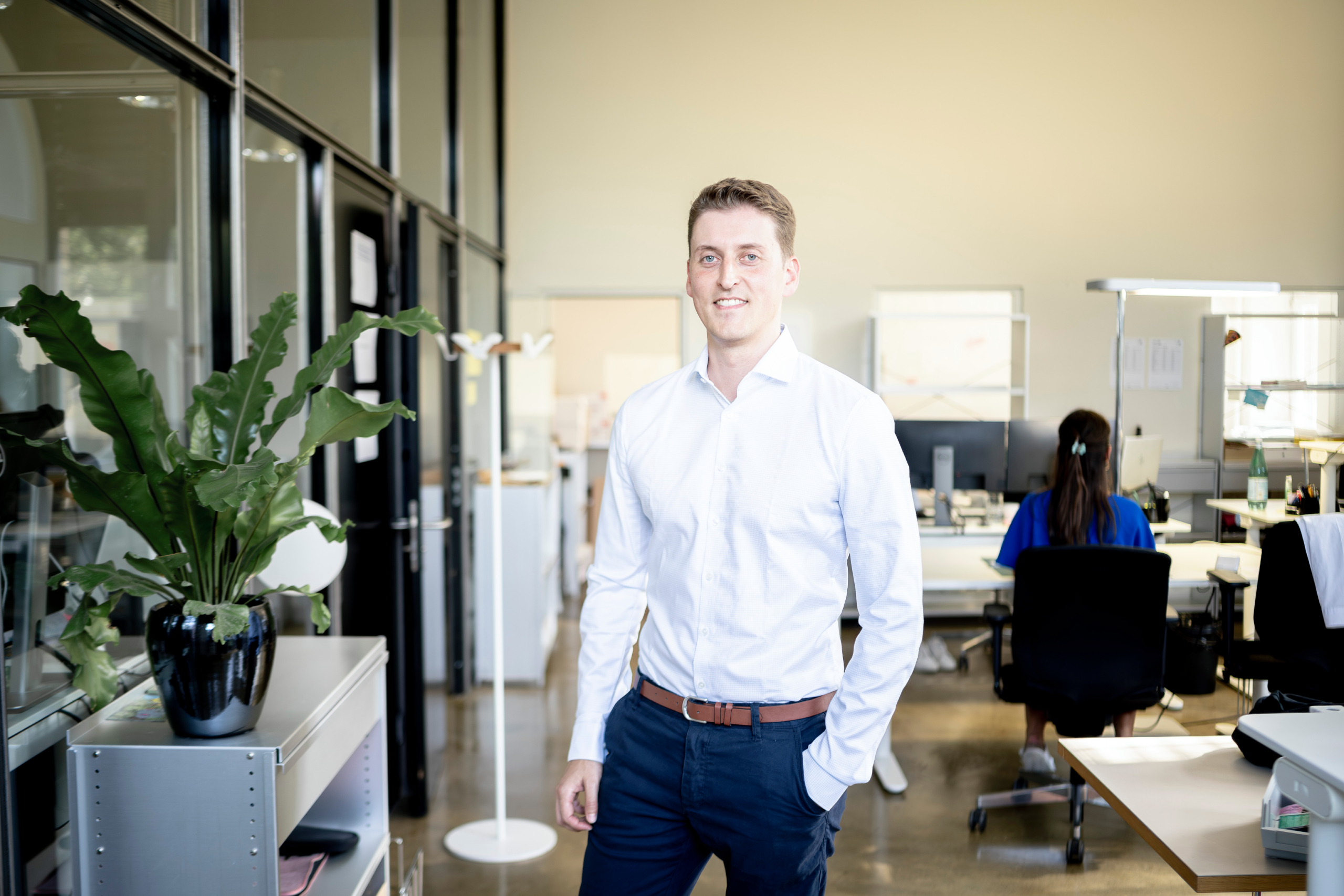 Junger Mnan mit Hemd der in einem Büro steht und in die Kamera schaut. 
