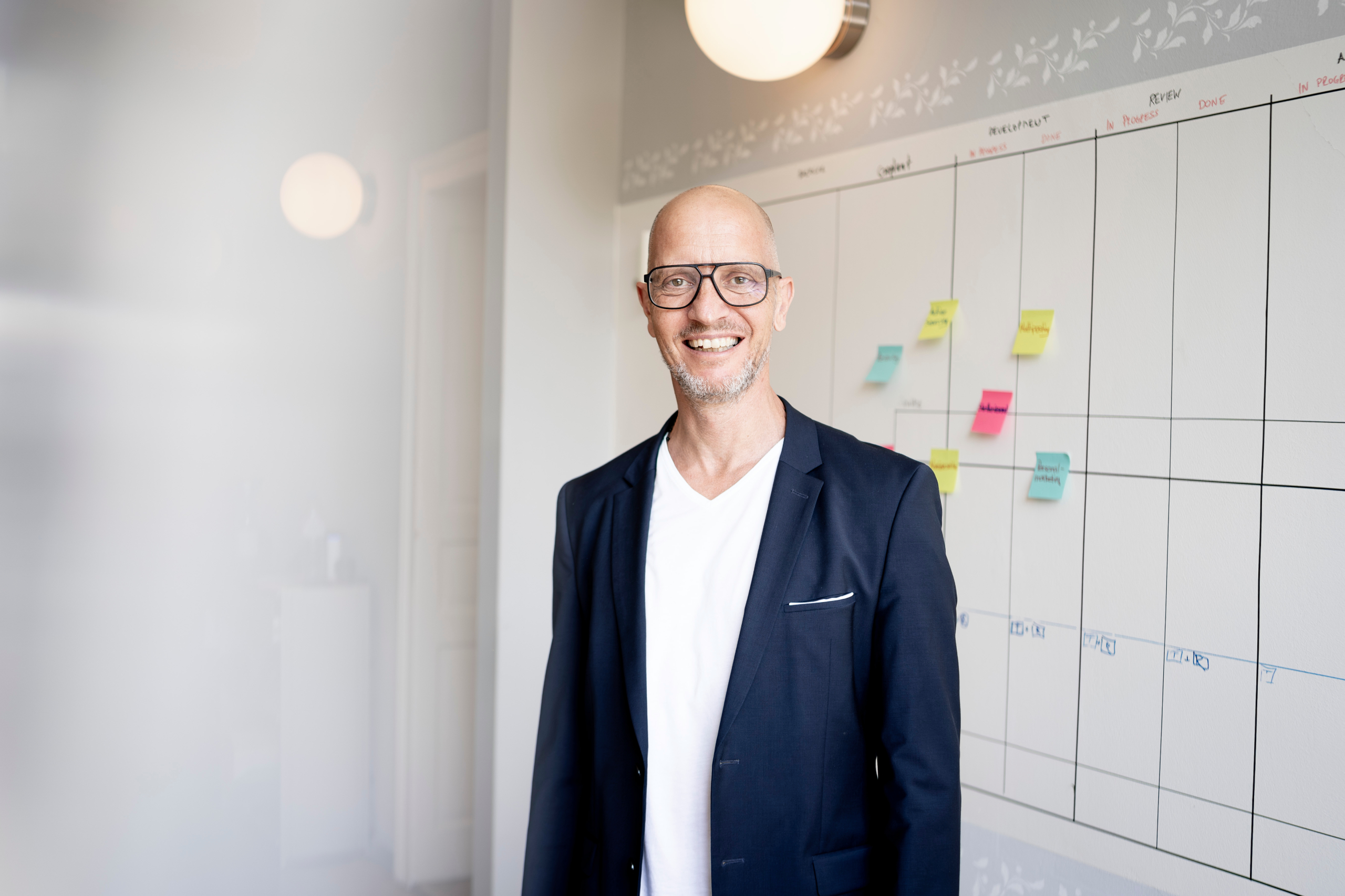 Mann im weissen Hemd und schwarzem Blazer der vor einer weissem Whiteboard steht.
