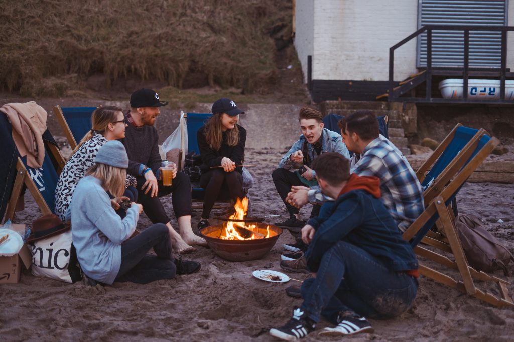 Menschengruppe sitzt am offenen Feuer am Strand und spricht.