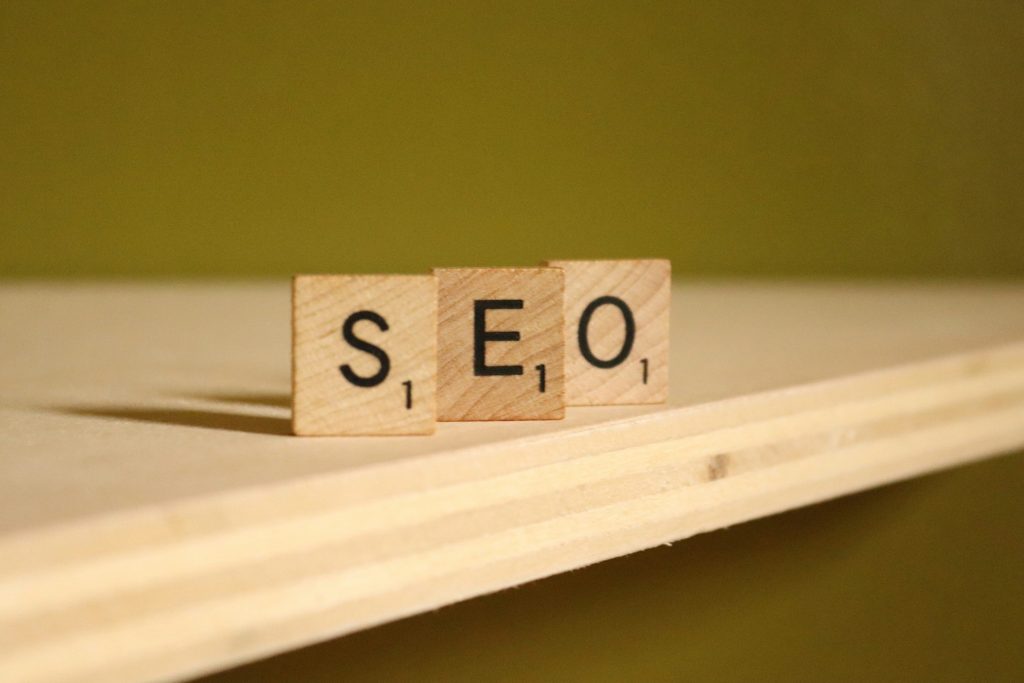 Holzspielsteine mit Buchstaben darauf, die das Wort "SEO" buchstabieren, liegen auf einer Holzoberfläche. Symbolbild für SEO bei Stellenanzeigen.